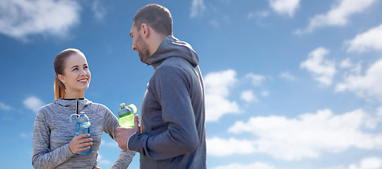 Image showing smiling couple with bottles of water over blue sky