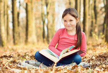 Image showing Little girl is reading a book outdoors