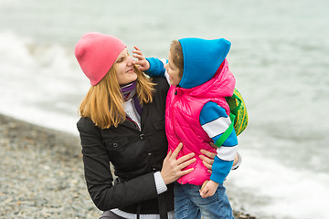 Image showing Little girl having fun touches mothers nose in warm clothes on the beach