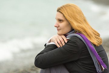 Image showing Portrait of enigmatic smiling girl on the background of the surf on a cloudy cold day