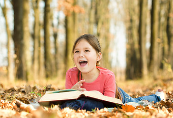 Image showing Little girl is reading a book outdoors