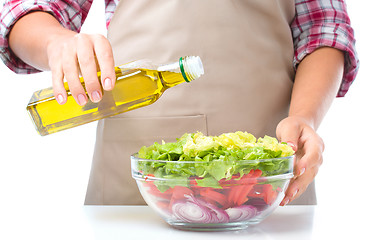 Image showing Cook is pouring olive oil into salad