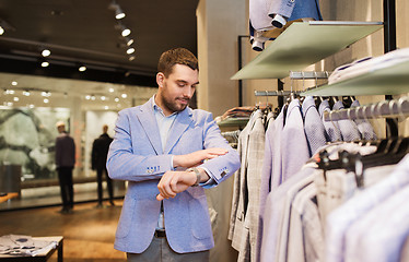 Image showing happy young man trying jacket on in clothing store