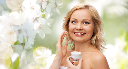 Image showing happy woman applying cream to her face