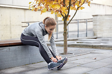 Image showing happy young sporty woman tying shoelaces outdoors