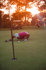 Image showing golf player blowing ball in hole with sunset in background