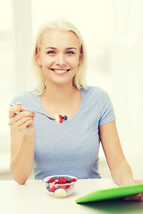 Image showing smiling woman eating fruits with tablet pc at home