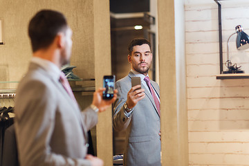 Image showing man in suit taking mirror selfie at clothing store