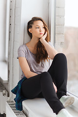 Image showing sad pretty teenage girl sitting on windowsill