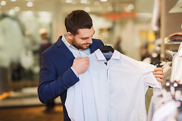 Image showing happy young man choosing clothes in clothing store