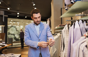 Image showing happy young man trying jacket on in clothing store