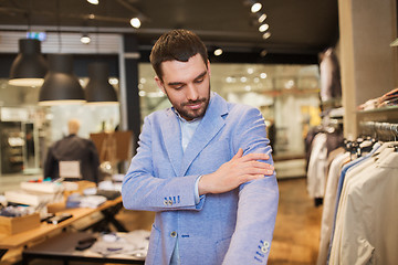 Image showing happy young man trying jacket on in clothing store