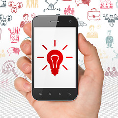 Image showing Business concept: Hand Holding Smartphone with Light Bulb on display