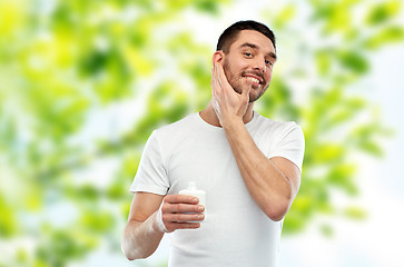 Image showing happy young man applying cream or lotion to face