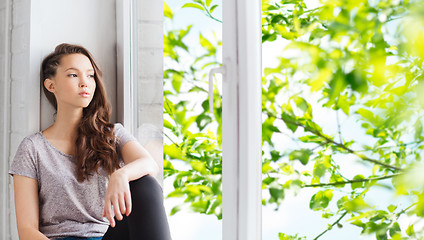 Image showing sad pretty teenage girl sitting on windowsill