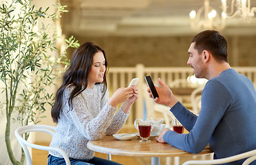Image showing happy couple with smartphones drinking tea at cafe