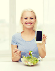 Image showing smiling woman with smartphone eating salad at home