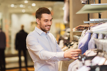 Image showing happy young man choosing clothes in clothing store