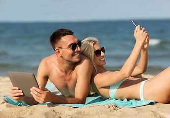 Image showing happy couple with modern gadgets lying on beach