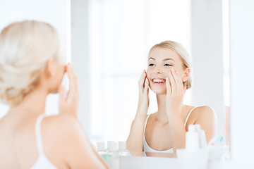 Image showing happy woman applying cream to face at bathroom