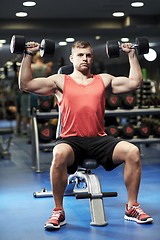 Image showing young man with dumbbells flexing muscles in gym