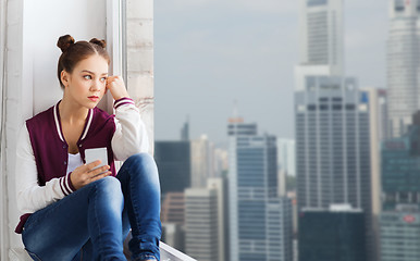 Image showing teenage girl sitting on windowsill with smartphone