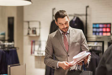 Image showing happy young man choosing shirt in clothing store