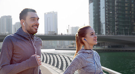 Image showing happy couple with earphones running in city