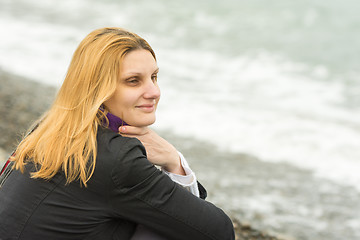 Image showing A girl sits on the beach on a cloudy day in cold weather and looking thoughtfully into the distance