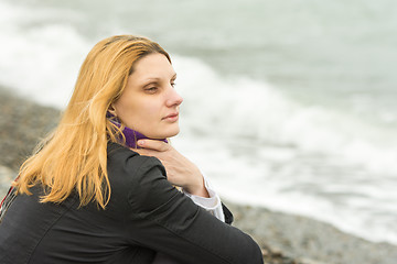 Image showing A girl sits on the beach on a cloudy day in cold weather and looking thoughtfully into the distance