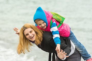 Image showing Close-up of a young girl playing with her baby on the nature near the water in cold weather