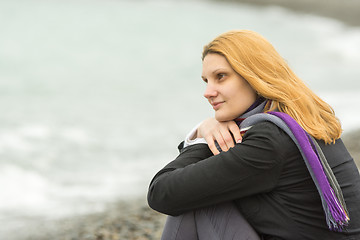 Image showing Portrait of sitting girl on the beach on a cloudy cold day put his head in his hands