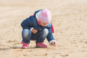 Image showing Five-year girl in the spring of the pen draws on the sand by the sea