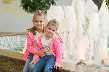 Image showing Two girls sitting at the fountain in the mall and joyfully look to the Frame
