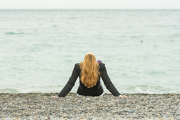 Image showing She sits back on a pebble beach by the sea on a cloudy day, his head thrown back