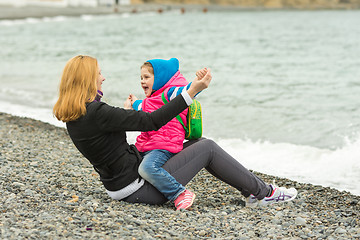 Image showing Mom and daughter having fun playing while sitting on the beach on a cool day