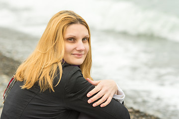 Image showing Portrait of sitting on the beach mysteriously smiling girl in cloudy weather