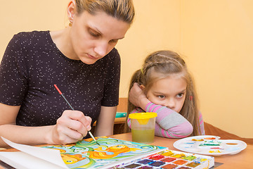 Image showing The girl-artist draws on the colors of paper next to a little girl with a bored look