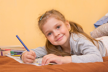 Image showing Cheerful little girl draws lying on his stomach with a pencil on paper