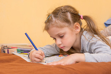 Image showing Little girl draws a hard lying on his stomach with a pencil on paper