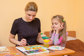 Image showing A little girl is watching carefully for a teacher who shows how to paint watercolor