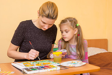 Image showing Girl artist teaches a little girl at the table as a draw watercolor on paper