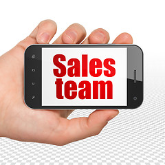 Image showing Advertising concept: Hand Holding Smartphone with Sales Team on display