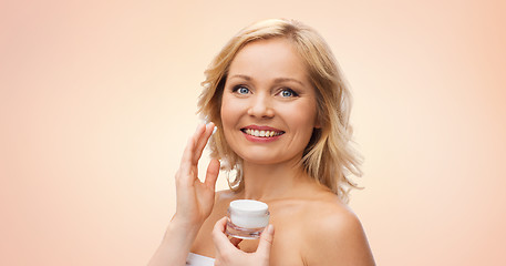 Image showing happy woman applying cream to her face