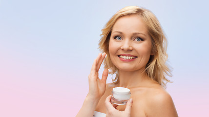 Image showing happy woman applying cream to her face