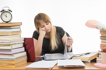 Image showing Student sadly looking at turning the pages in a folder at the desk among the stacks of books