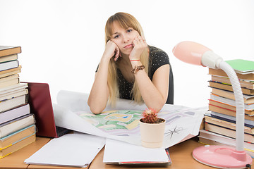 Image showing The girl is sad student sitting at a table crammed with books, drawings