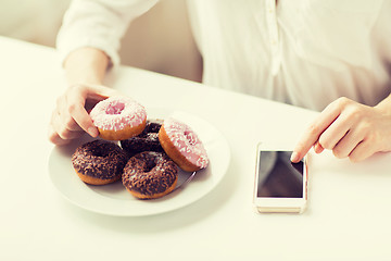 Image showing close up of hands with smart phone and donuts