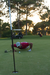 Image showing golf player blowing ball in hole with sunset in background