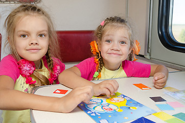 Image showing Two little sisters in the train of fun playing at the table at the lower place in the second-class compartment wagon